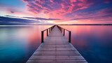 Fototapeta Perspektywa 3d - a wooden dock extending into calm waters, with a  colorful sky at dusk or dawn in the background.