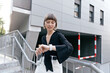 © PhotoBook - Excited stylish fairly with short hair is checking her smart watch on modern city building