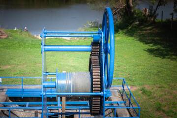 Picture of a cogwheel mechanism in front of a river in a natural environment.