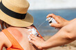 Mother applying sunburnt  relief spray to her child at a beach