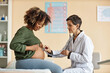 © Seventyfour - Side view of young pregnant African American woman looking at her big bare belly while senior Caucasian gynecologist checking baby with stethoscope in modern clinic