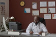 © AnnaStills - African american doctor sitting alone at his office desk and working with documents