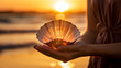 Hand holding a fish ear shell against the backdrop of a coastal sunrise