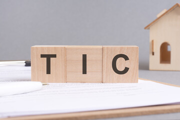 Poster - tic text made of wooden blocks on gray background with a small wooden model house