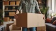© Anna - moving concept, a man stands among cardboard boxes with things and furniture in the middle of an empty living room and opens packed boxes