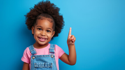 Wall Mural - young African American girl with a big smile, wearing a pink shirt and a blue denim jumper, set against a light blue background