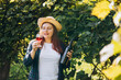 © mdyn - 30s Woman in hat tasting red wine in vineyard. Portrait of pretty young woman holding glass of wine and bottle of wine. Mockup for design, Natural wine industry.