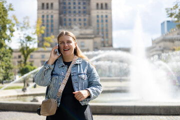 Wall Mural - Lifestyle portrait of a stylish young 30s woman talking on cell phone, making call on city street. Urban lifestyle concept. 30s female relaxing outdoors