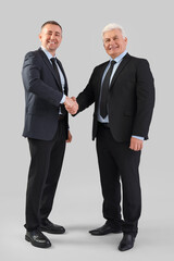 Poster - Mature brothers in suits shaking hands on grey background