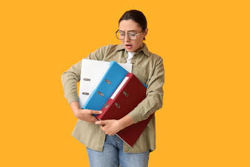 Canvas Print - Stressed young businesswoman with document folders on yellow background