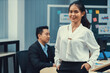 © Summit Art Creations - Successful businesswoman in white uniform standing in modern office in confident poses while smiling. Portrait of asian woman with arms akimbo. her partner working on laptop computer Intellectual.