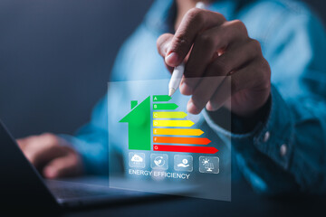 Businessman use laptop with virtual screen of energy efficiency rating for energy efficient house building rate label audit. Energy efficiency concept.