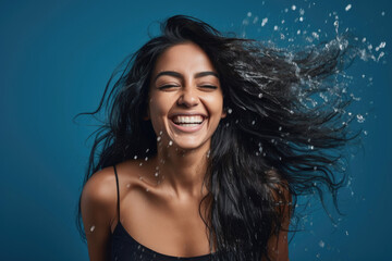 Wall Mural - Studio portrait of a joyful young woman of Indian ethnicity having long flowing hair playing with water