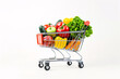 © L.S. - miniature toy shopping cart filled with various vegetables against a white background