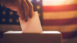 Close-up of a voter's hand placing a ballot into a voting box with the American flag in the background, symbolizing democratic participation.