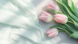 Fototapeta Tulipany - Light pink tulips rest on delicate white drapery, creating a serene and romantic atmosphere.