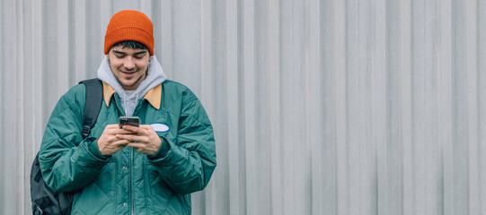 Wall Mural - young man with mobile phone on outdoor wall background wearing winter clothes