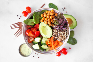 Wall Mural - Healthy homemade salad bowl with avocado, chickpeas, quinoa and vegetables. Overhead view with frame of ingredients on a white marble background.