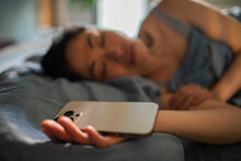 Young Woman Sleeping In Home Bed Holding Smartphone