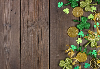 Poster - St Patricks Day side border of green shamrocks, gold coins and ribbon. Top view over a rustic dark wood background with copy space.
