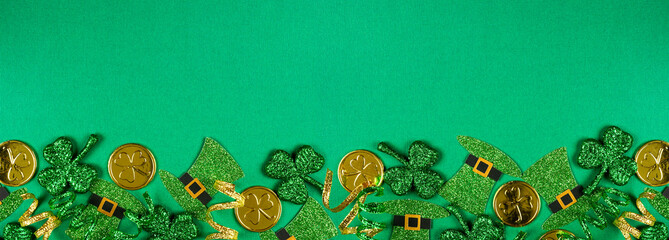 Poster - St Patricks Day bottom border of  shamrocks, leprechaun hats, gold coins and ribbon. Top view over a green banner background with copy space.