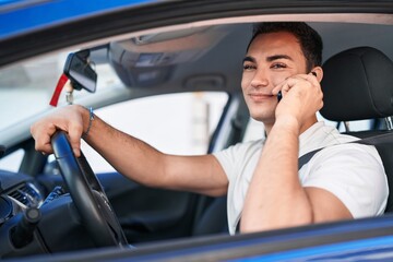 Sticker - Young hispanic man talking on smartphone sitting on car at street