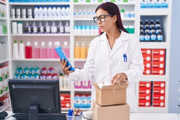 Wall Mural - Young beautiful hispanic woman pharmacist using touchpad holding pills bottle at pharmacy