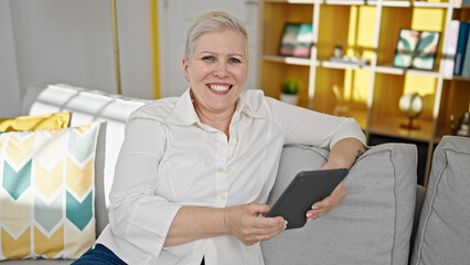 Wall Mural - Middle age grey-haired woman using touchpad sitting on sofa at home