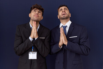 Sticker - Two hispanic business men wearing business clothes begging and praying with hands together with hope expression on face very emotional and worried. begging.