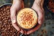 Hands hold freshly brewed cappuccino, sprinkled with chocolate shavings on foam, set over backdrop of rich coffee beans, invite experience of comfort and exquisite taste for coffee aficionado