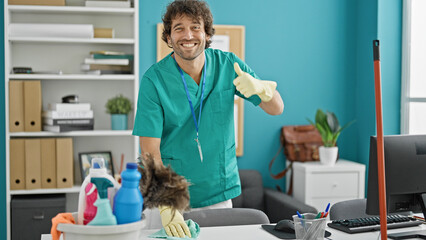 Wall Mural - Young hispanic man cleaning table with a cloth doing thumb up gesture at office