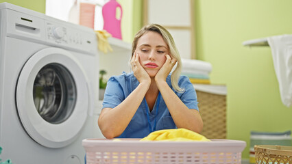 Canvas Print - Young blonde woman professional cleaner tired leaning on basket with clothes at laundry room