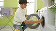 © Krakenimages.com - Smiling young hispanic teenager enjoying doing laundry, confidently inserting detergent bag into washing machine in laundry room