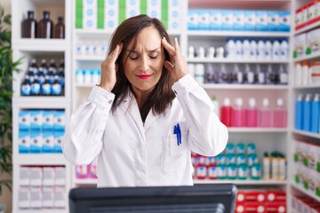 Poster - Middle age brunette woman working at pharmacy drugstore with hand on head for pain in head because stress. suffering migraine.