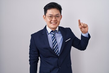 Sticker - Young asian man wearing business suit and tie smiling and confident gesturing with hand doing small size sign with fingers looking and the camera. measure concept.