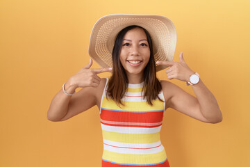 Wall Mural - Middle age chinese woman wearing summer hat over yellow background smiling cheerful showing and pointing with fingers teeth and mouth. dental health concept.