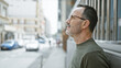 © Krakenimages.com - Serious, middle age man with grey hair, glasses, and a beard stands outdoors. as he looks up, his concentrated expression hints his thoughts are lost in the urban city street.