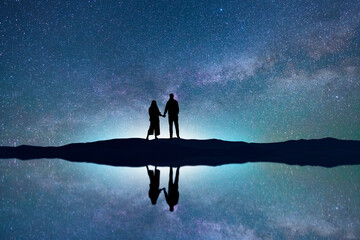 Wall Mural - couple lovers standing on the lake beach with reflection, on the milky way galaxy background.