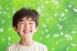 A young boy is smiling in front of a green background with white confetti falling around him.
