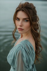 Canvas Print -  a woman in a blue dress standing in a body of water with her hair blowing in the wind and looking at the camera with a serious look on her face.