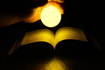 a man holds a luminous sphere in his hand above the pages of an open book in the dark. a glowing ball illuminates the pages. magic in the book  