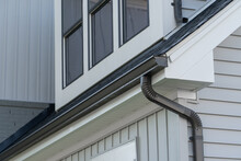 Dark Brown Frame Gutter Guard System, With White Horizontal And Vertical Vinyl Siding Fascia, Drip Edge, Soffit, On A Pitched Roof Attic At A Luxury American Single Family