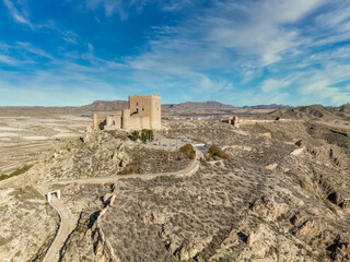 Canvas Print - Aerial view of Jumilla medieval castle in Murcia Spain, on a hilltop, imposing irregular shape keep with four floors, crenelated battlements cloudy blue sky background