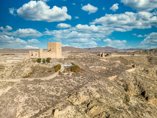 Poster - Aerial view of Jumilla medieval castle in Murcia Spain, on a hilltop, imposing irregular shape keep with four floors, crenelated battlements cloudy blue sky background