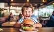 Little cute boy eating a sandwich in a cafe, concept of a childrens fast food meal