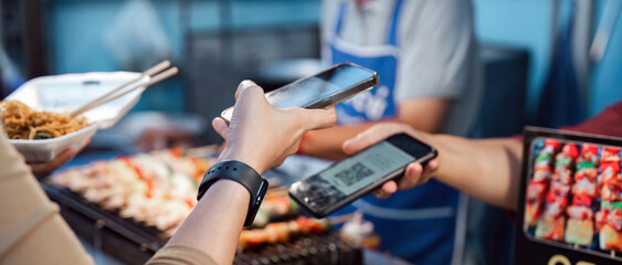 asian traveler paying contactless with mobile phone in street food night market. mobile payment conc