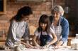 © fizkes - Hands in flour. Friendly intergenerational family of 3 diverse age females engaged in cooking short pastry biscuits. Young mom senior granny assist little girl stretch dough for pie on kitchen table