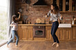 Active leisure. Joyful latin mother cute preteen daughter dance jump barefoot sing have fun at modern kitchen with floor heating. Energetic small child young mom celebrate getting mortgage moving day