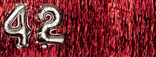 Silver Foil Balloon Number 42 On A Background Of Red Tinsel Decoration. Birthday Greeting Card, Inscription Forty-two. Anniversary Event. Banner.