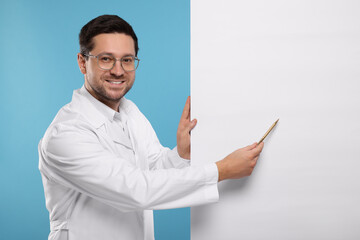 Canvas Print - Ophthalmologist pointing at blank banner on light blue background, space for text